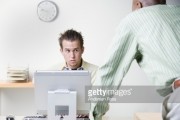 Businessman leaning on desk talking to coworker 