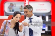 Smiling salesman showing woman cell phone in electronics store 