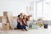 Young couple in new flat with cardboard boxes, sitting on floor 